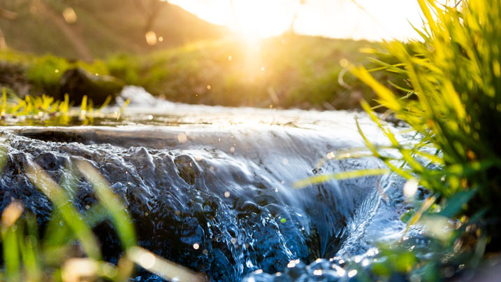 Close up of river flowing into a mini waterfall in glorious sunshine