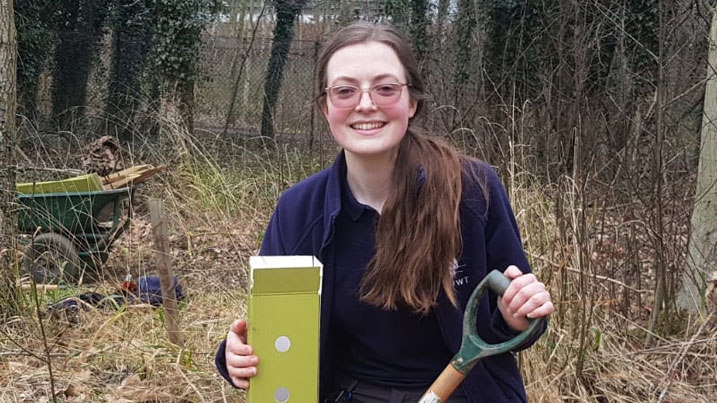 Head and shoulders of Kate, volunteer placement, out on the reserve, holding a spade