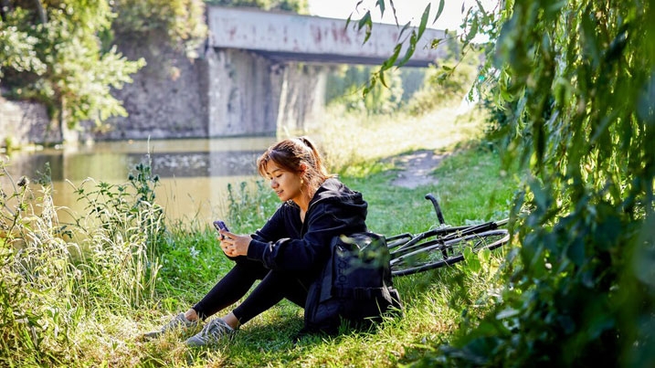 A young woman sitting by a river, checking her phone