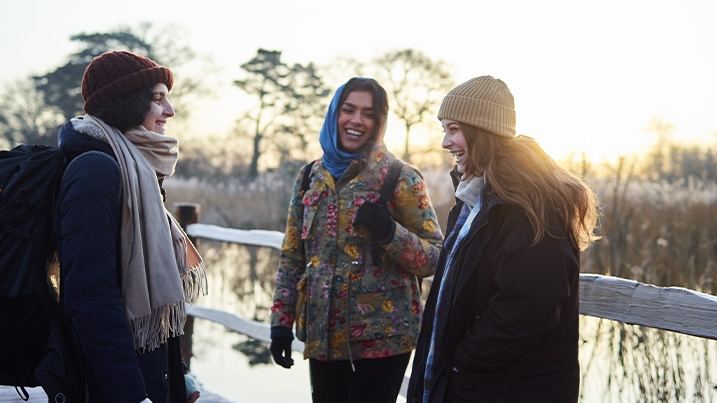 Three young women laughing and smiling at each other in a wintery outdoor setting