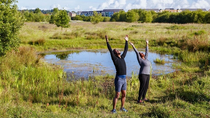 Two people practising yoga outside by a wetland in the sunshine