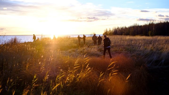 The sun setting against the sky over the wetlands. A group of people walk across the field.