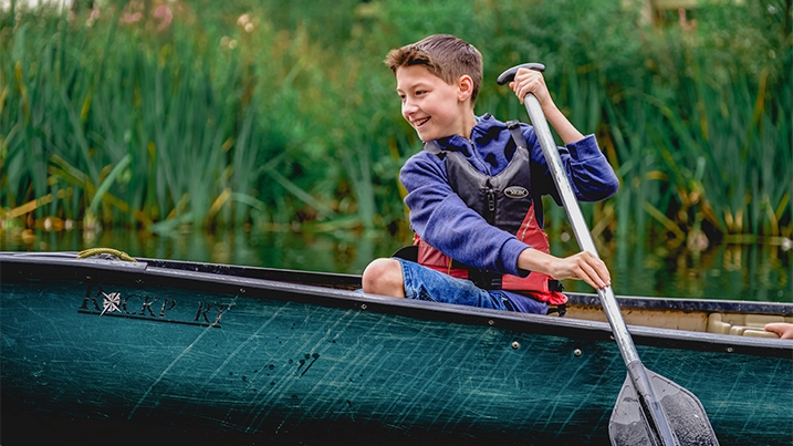 A child in a green canoe paddling through reeds