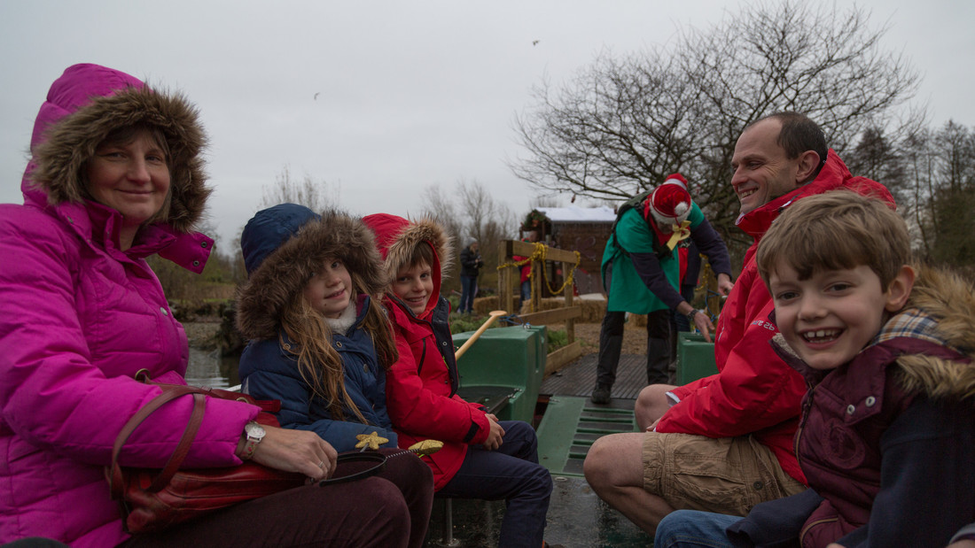 A family on board a boat to Santas Island. An elf is in the background securing the boat for them to get on to the island