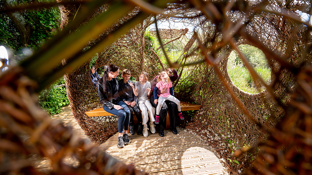 people sitting on a bench inside a room made of woven tree branches