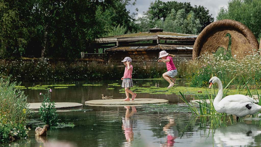 Young visitors jumping between stepping stones in the Estuary Shoreline garden at WWT Slimbridge