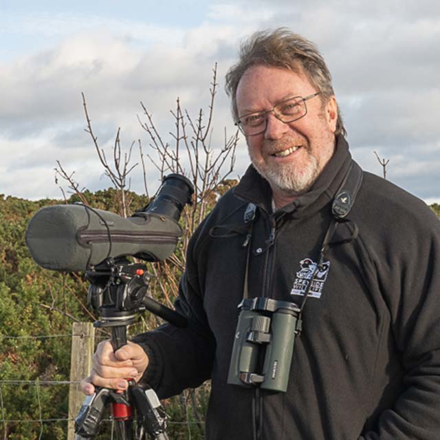 Roy Atkins of Speyside Wildlife stand with a telescope and binoculars, smiling at the camera