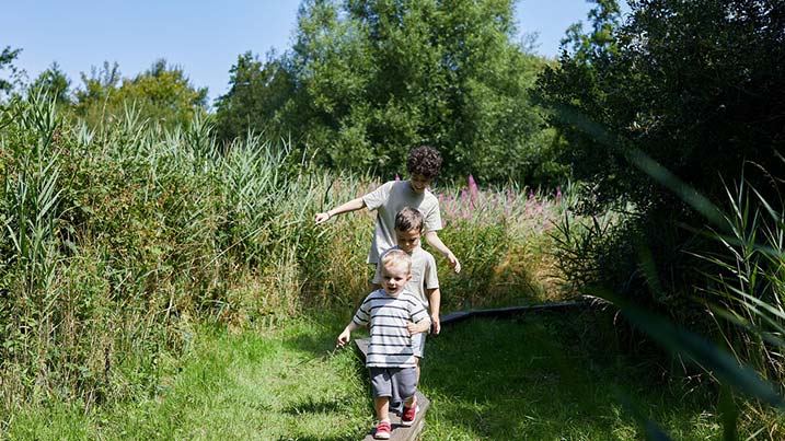 Three children following a wild play trail, along a balance beam