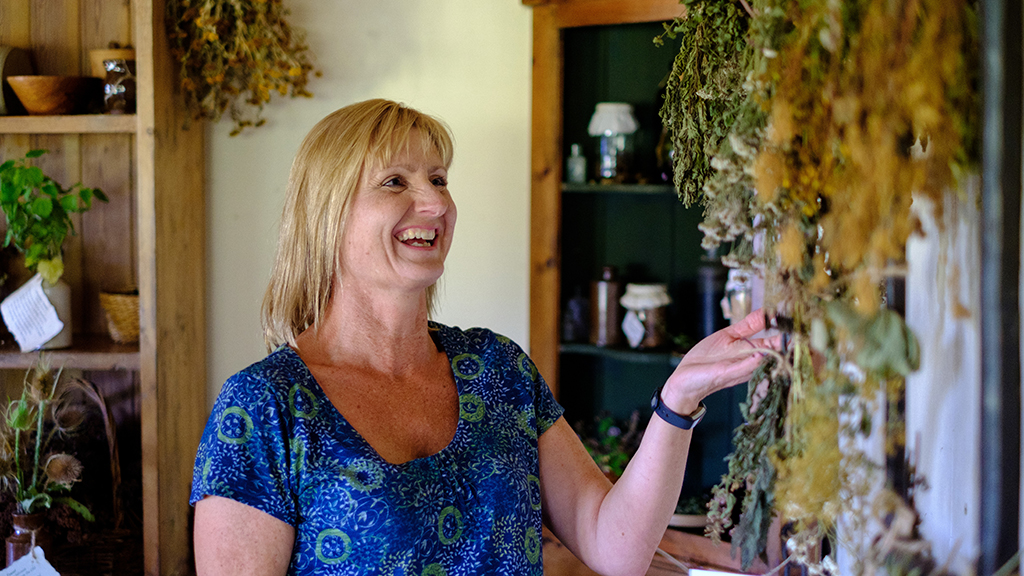 A woman touching drying herbs and flowers inside  