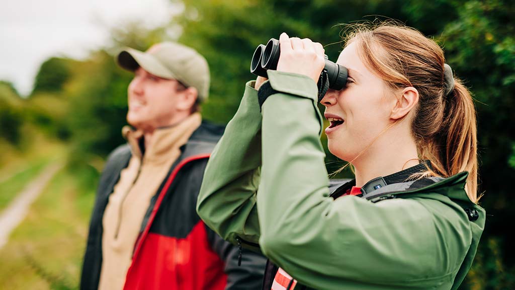 Visitors at WWT Caerlaverock, using binoculars to wildlife watch on one of the wildlife trails