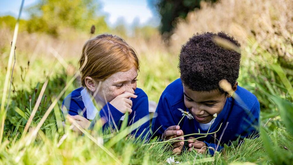Two children lie in grass while smiling