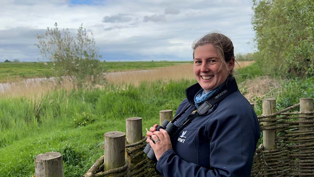 Lizzie Bruce, Site Manager at WWT Welney smiles at camera with the reserve in the background